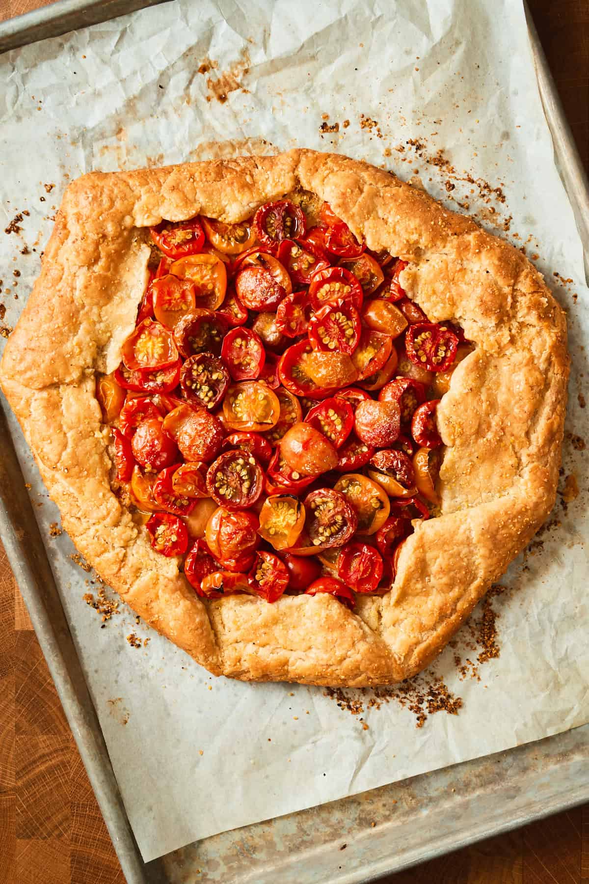 Baked tomato galette with a deep golden crust and roasted cherry tomatoes on a parchment-lined sheet pan.