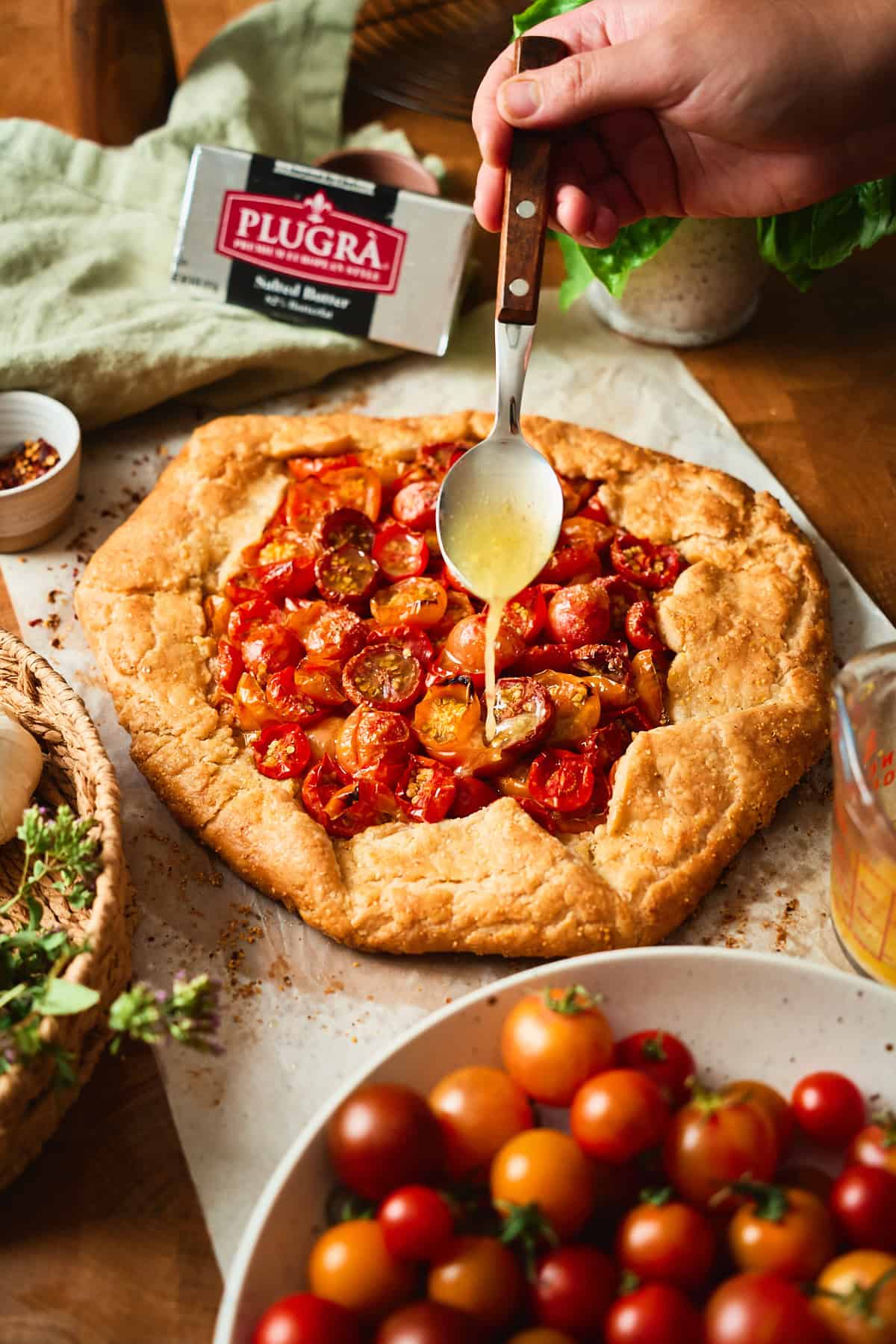 Lemon butter spooned over a baked tomato galette next to a package of Plugrà salted butter.