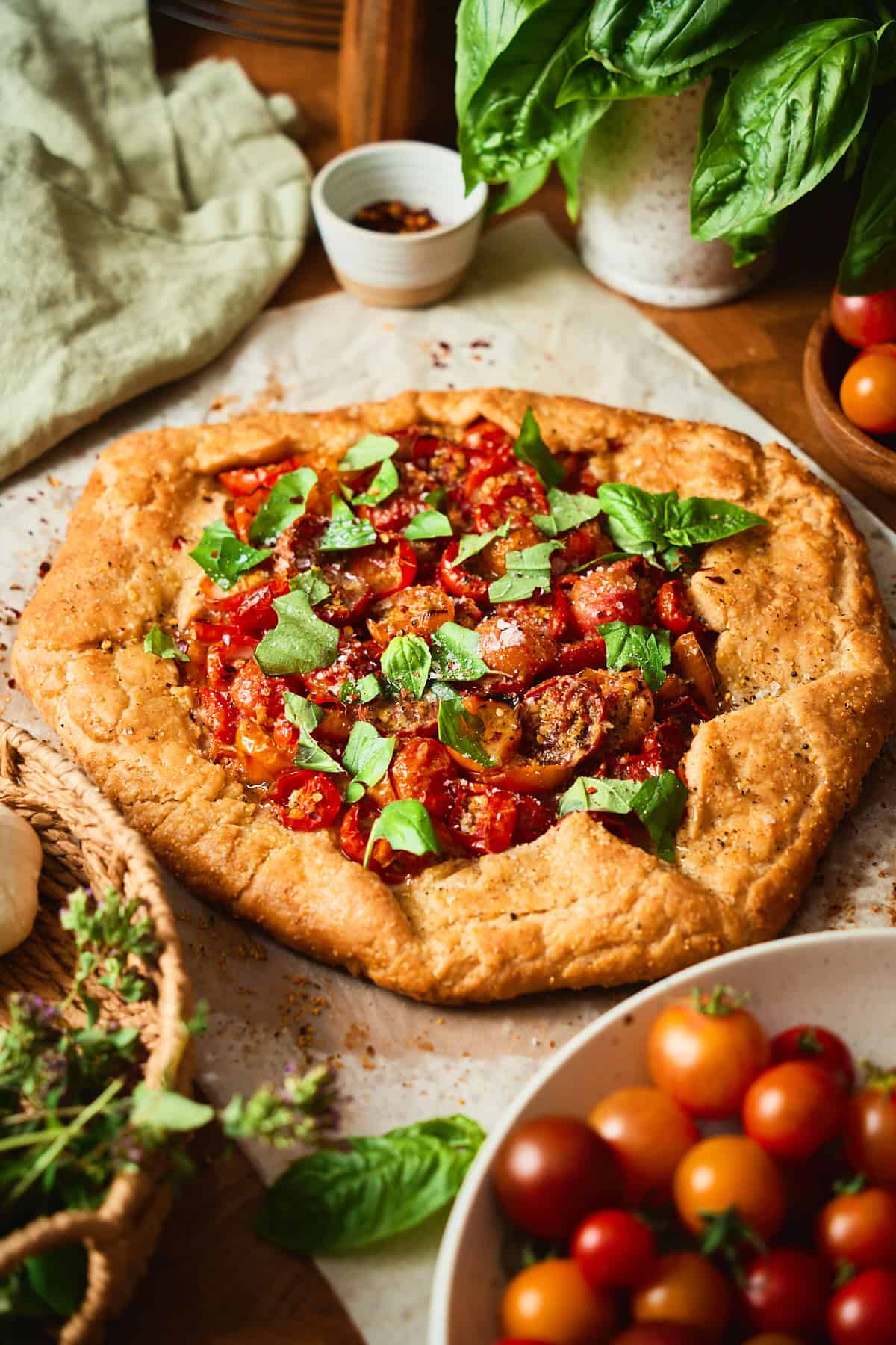 Tomato galette topped with torn basil and flaky salt, showing the golden pleated crust and roasted cherry tomato filling.