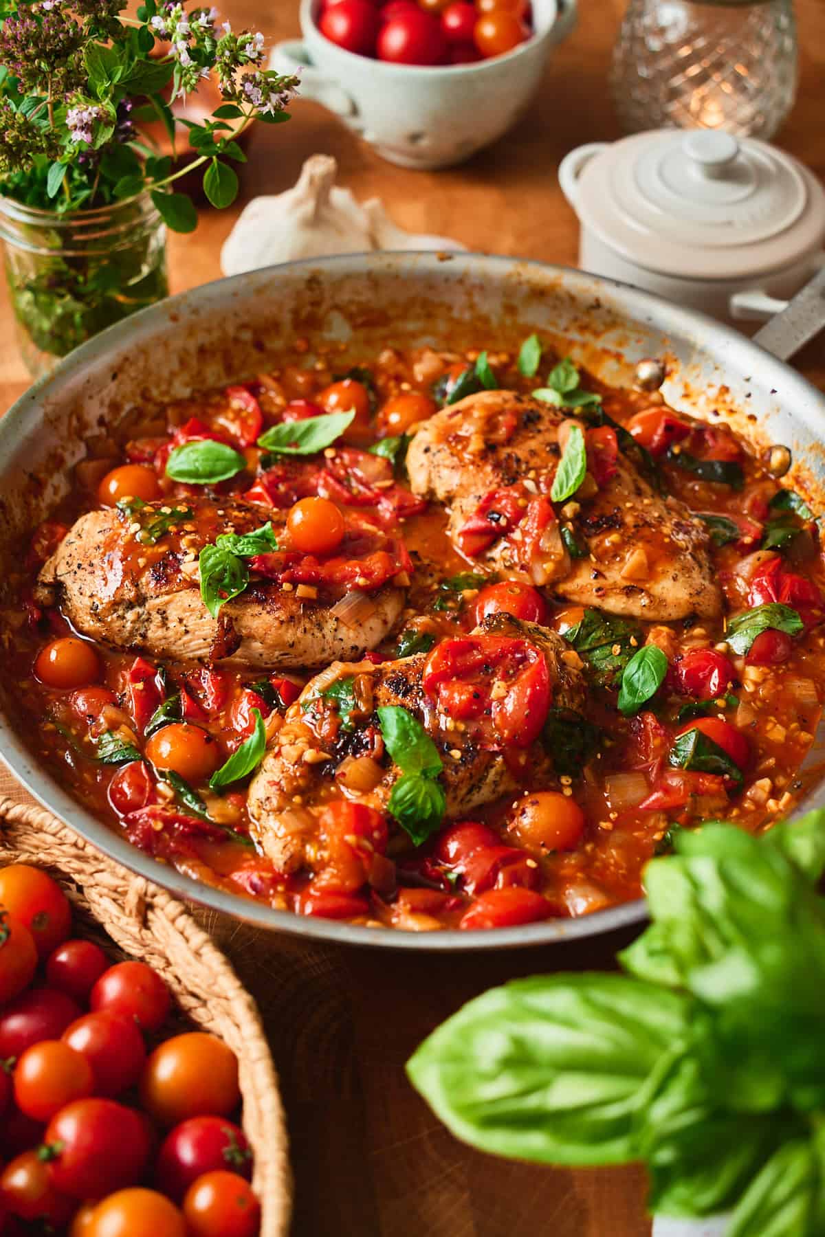 Chicken pomodoro in a skillet with burst cherry tomatoes and torn basil, side view.