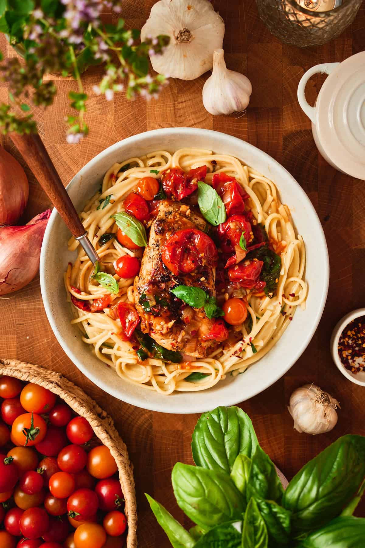 Chicken pomodoro served over linguine in a shallow bowl with fresh basil.