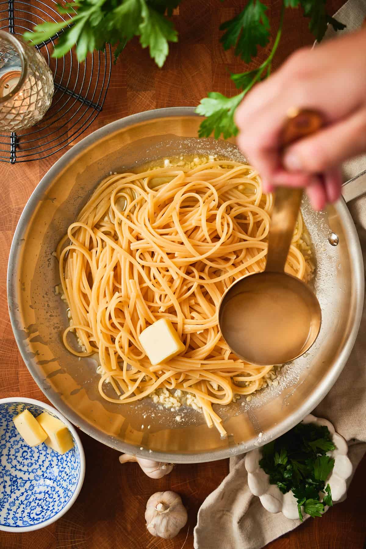 Ladling starchy pasta water over linguine and a pat of butter in the skillet.