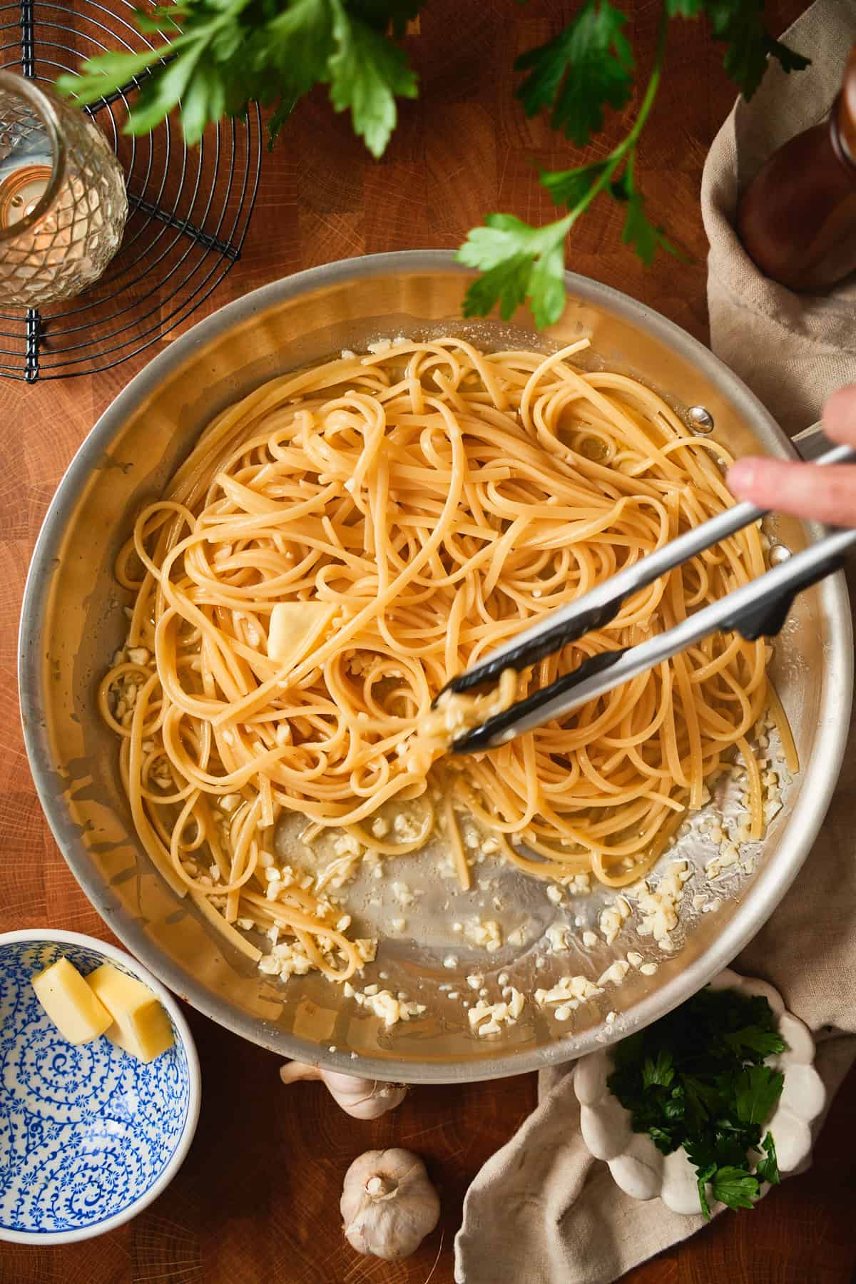 Tongs tossing linguine through garlic butter and pasta water in the skillet.