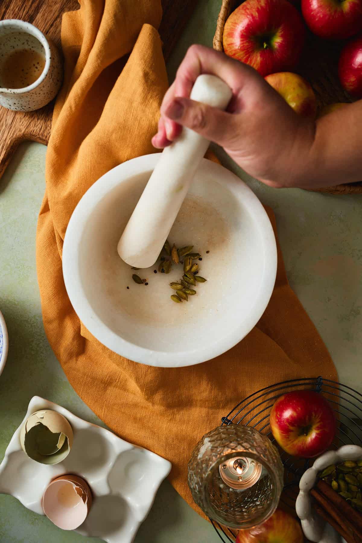 Green cardamom pods in a marble mortar with a pestle.