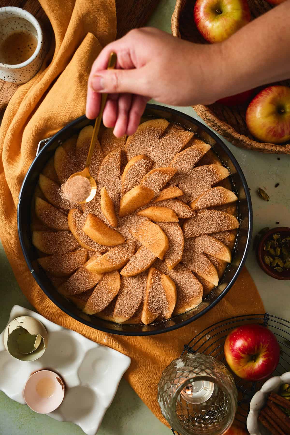 Hand sprinkling cinnamon sugar over arranged apple wedges.