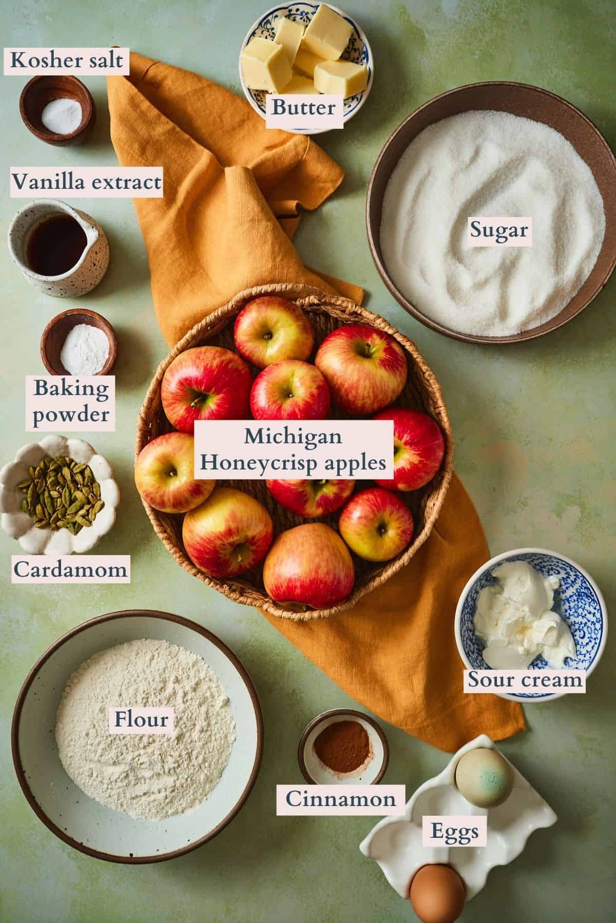 Ingredients for Swedish apple cake: apples, flour, sugar, butter, sour cream, eggs, cardamom pods, and cinnamon. Flat lay