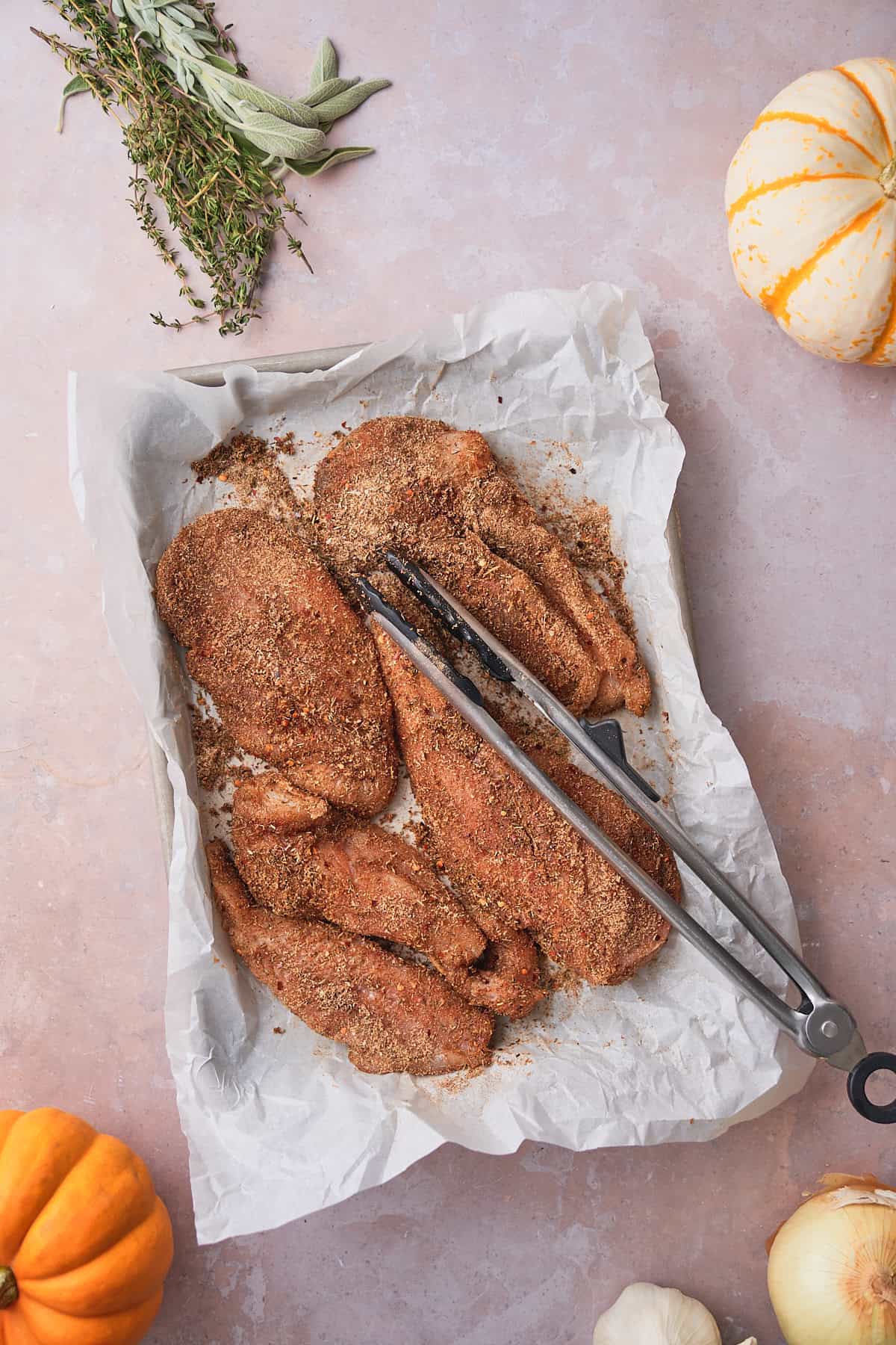 Chicken cutlets coated in a dry spice rub on parchment paper, with tongs resting alongside.