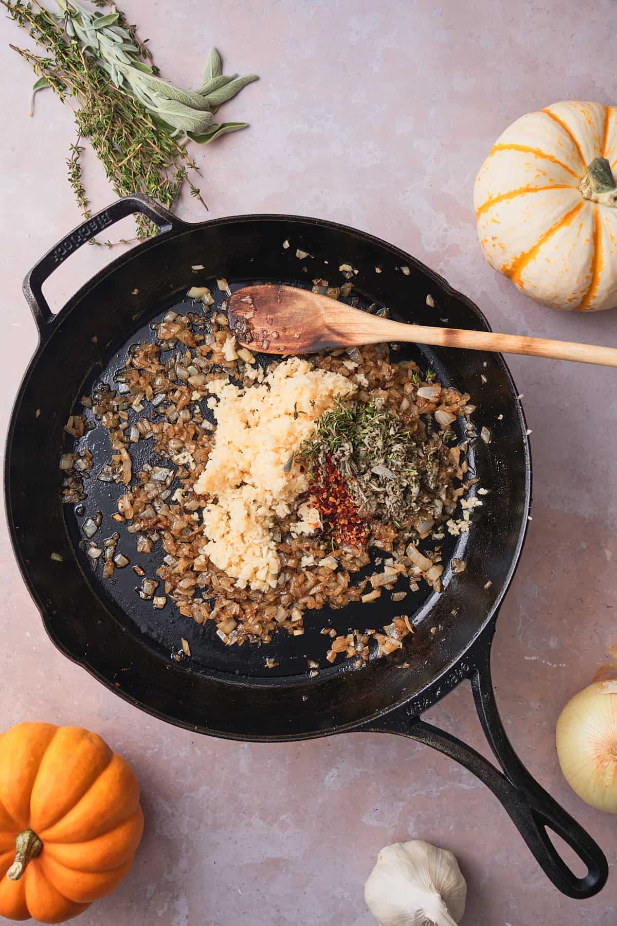 Softened onions in a cast iron skillet with minced garlic, fresh thyme, dried sage, and red pepper flakes added on top.
