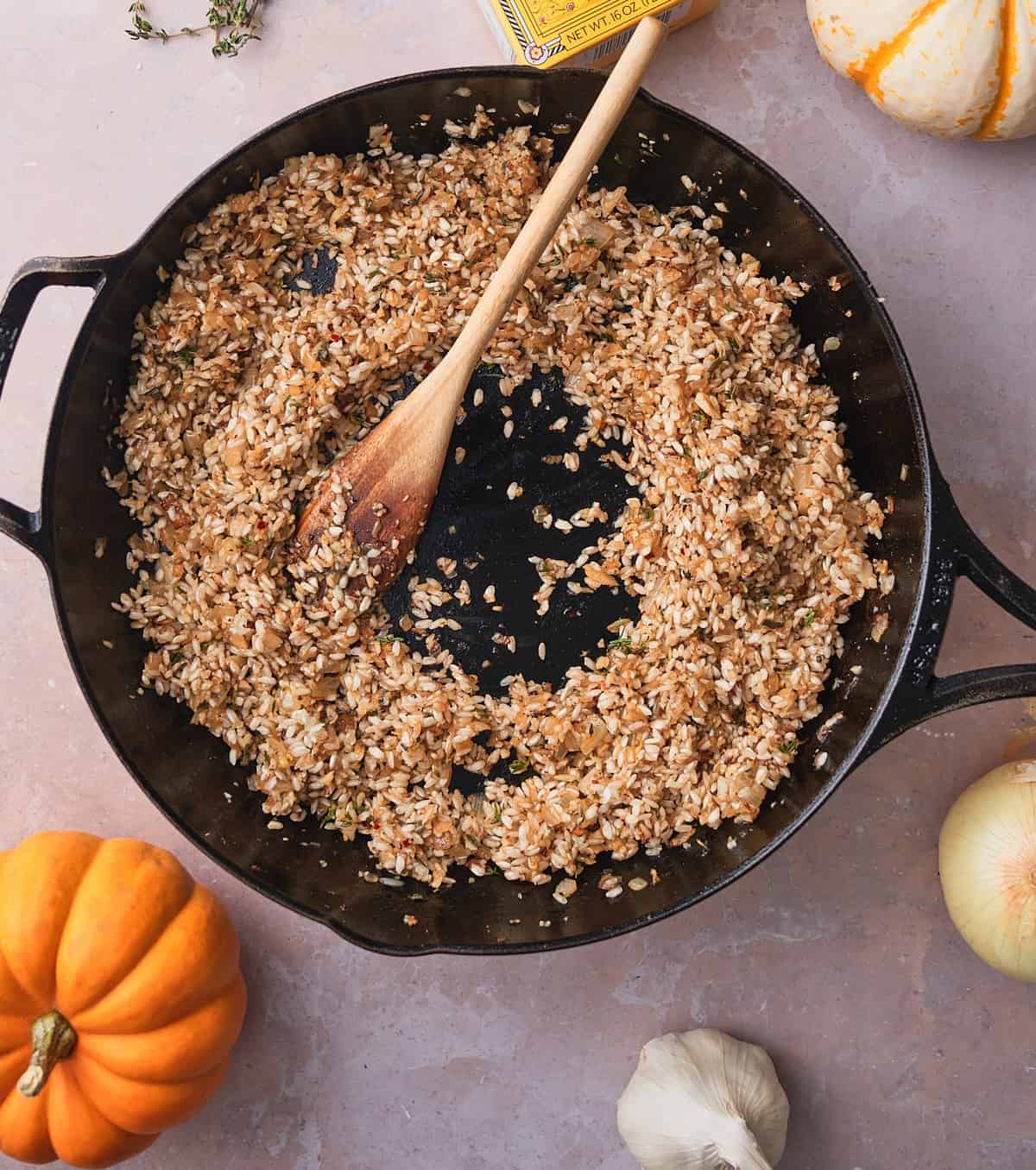 Arborio rice toasting with onions and garlic in a cast iron skillet, stirred with a wooden spoon.