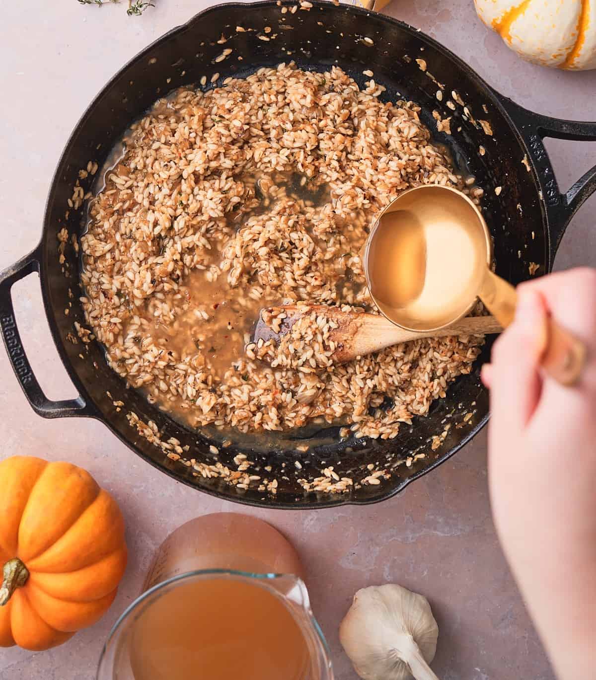 Warm chicken stock being ladled into a skillet of partly cooked risotto.