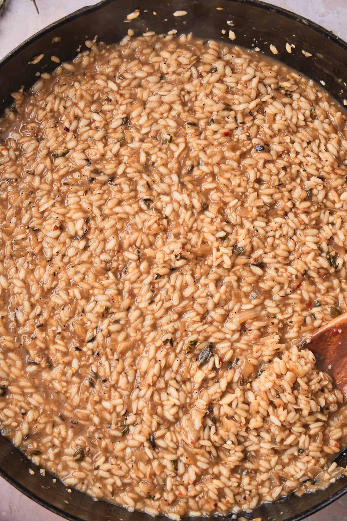 A wooden spoonful of creamy al dente risotto lifted above the skillet.