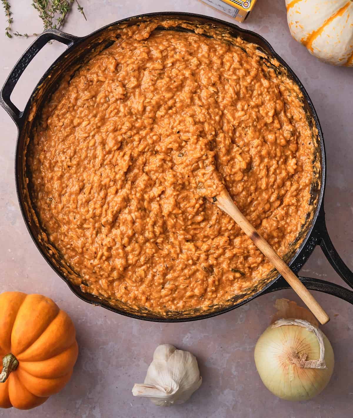 Finished pumpkin risotto in a cast iron skillet, deep orange and creamy, with a wooden spoon resting in it.