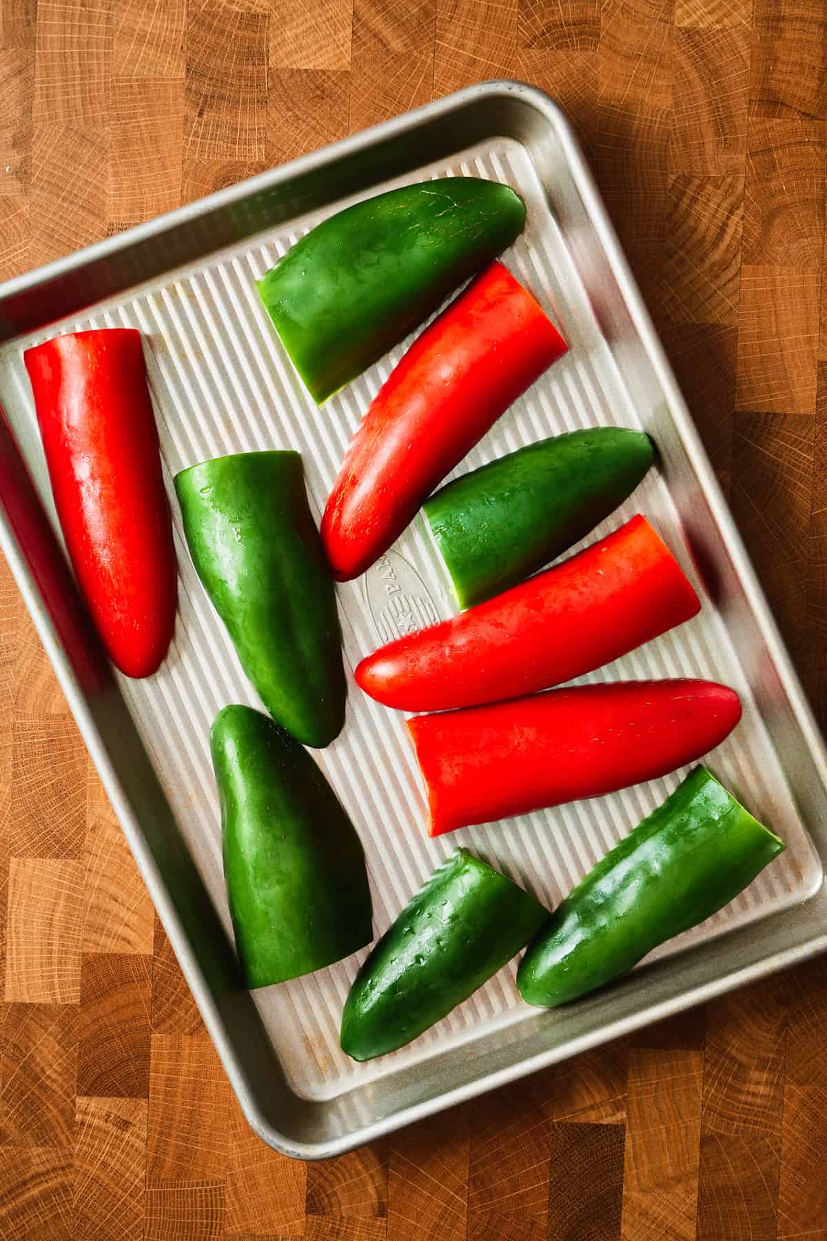 Halved red and green jalapeños arranged cut side down on a sheet pan before broiling.