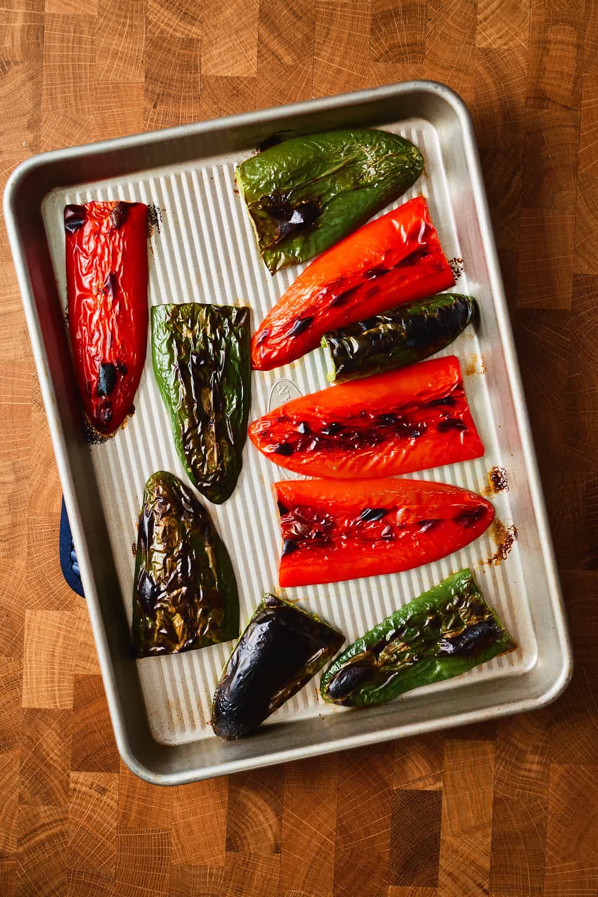 Broiled jalapeños with blackened, blistered skins on a sheet pan.