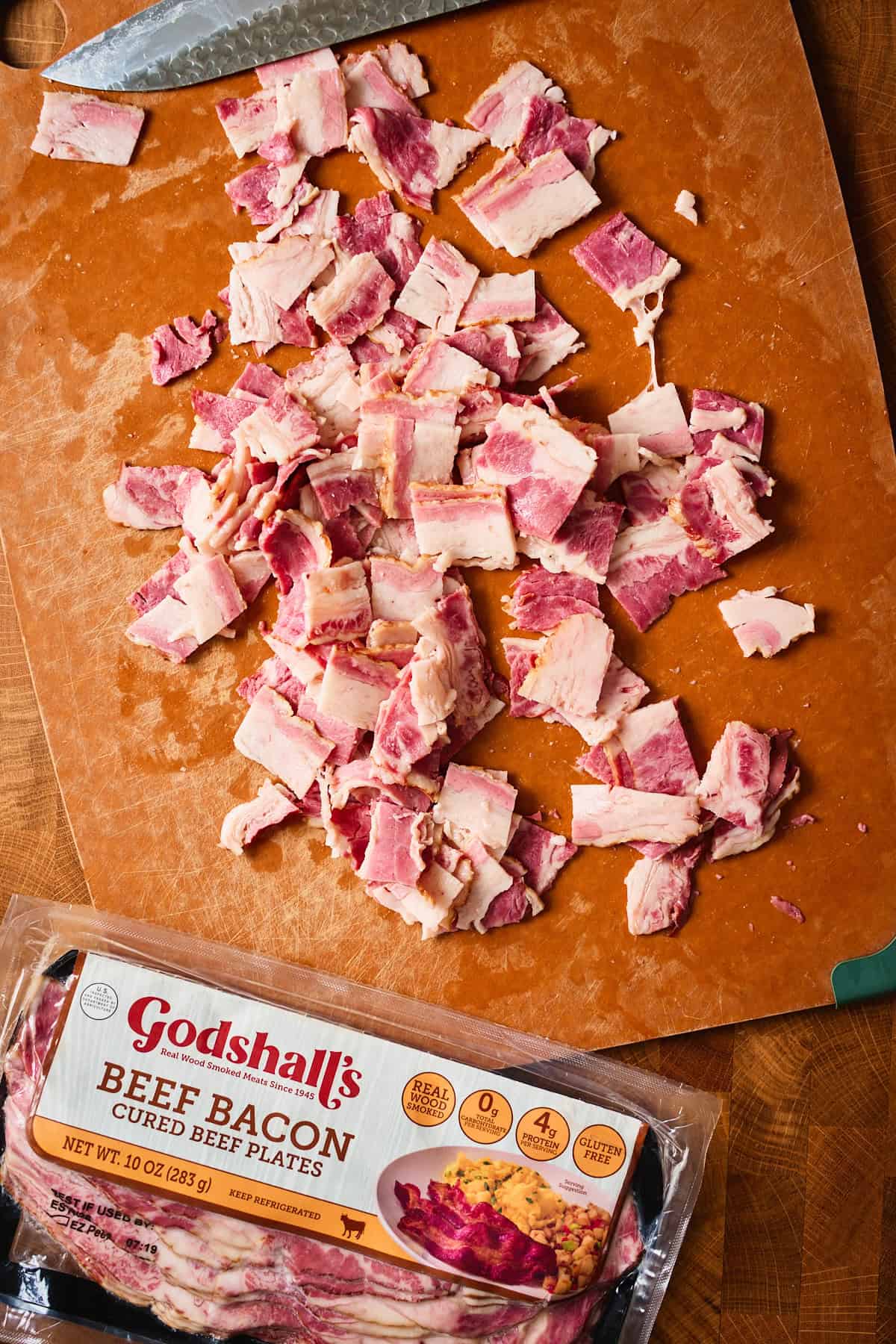 Diced Godshall's beef bacon on a cutting board next to the package.