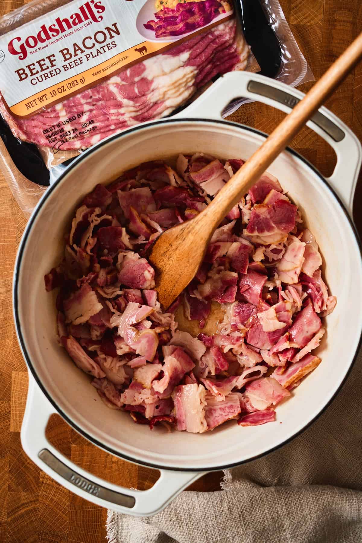 Diced beef bacon in a cold white Dutch oven before rendering.