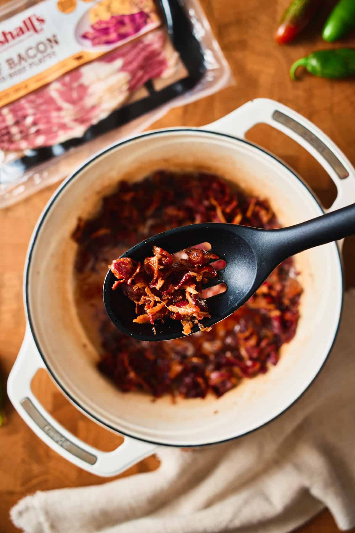 A slotted spoon lifting crispy beef bacon out of a Dutch oven.