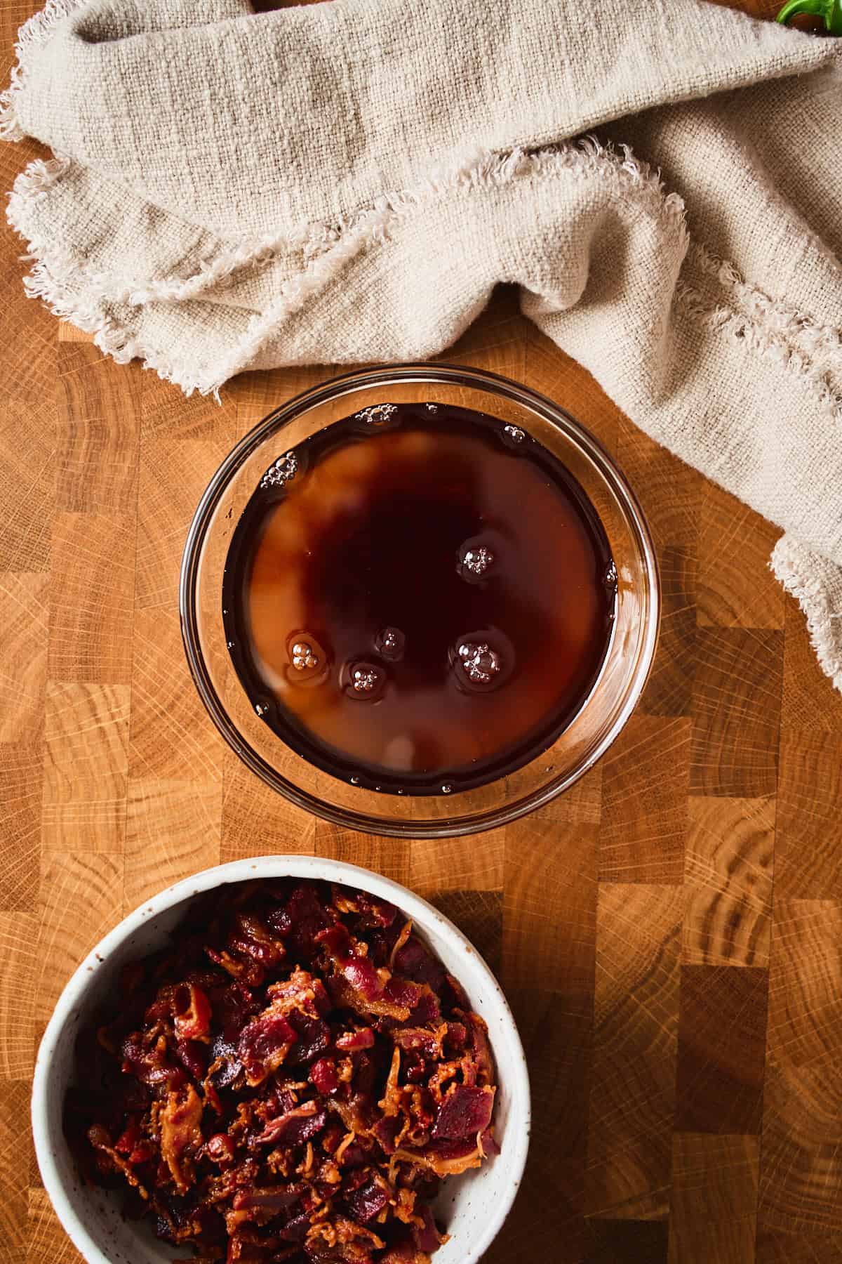 A glass bowl of rendered beef bacon fat next to a bowl of crispy beef bacon.