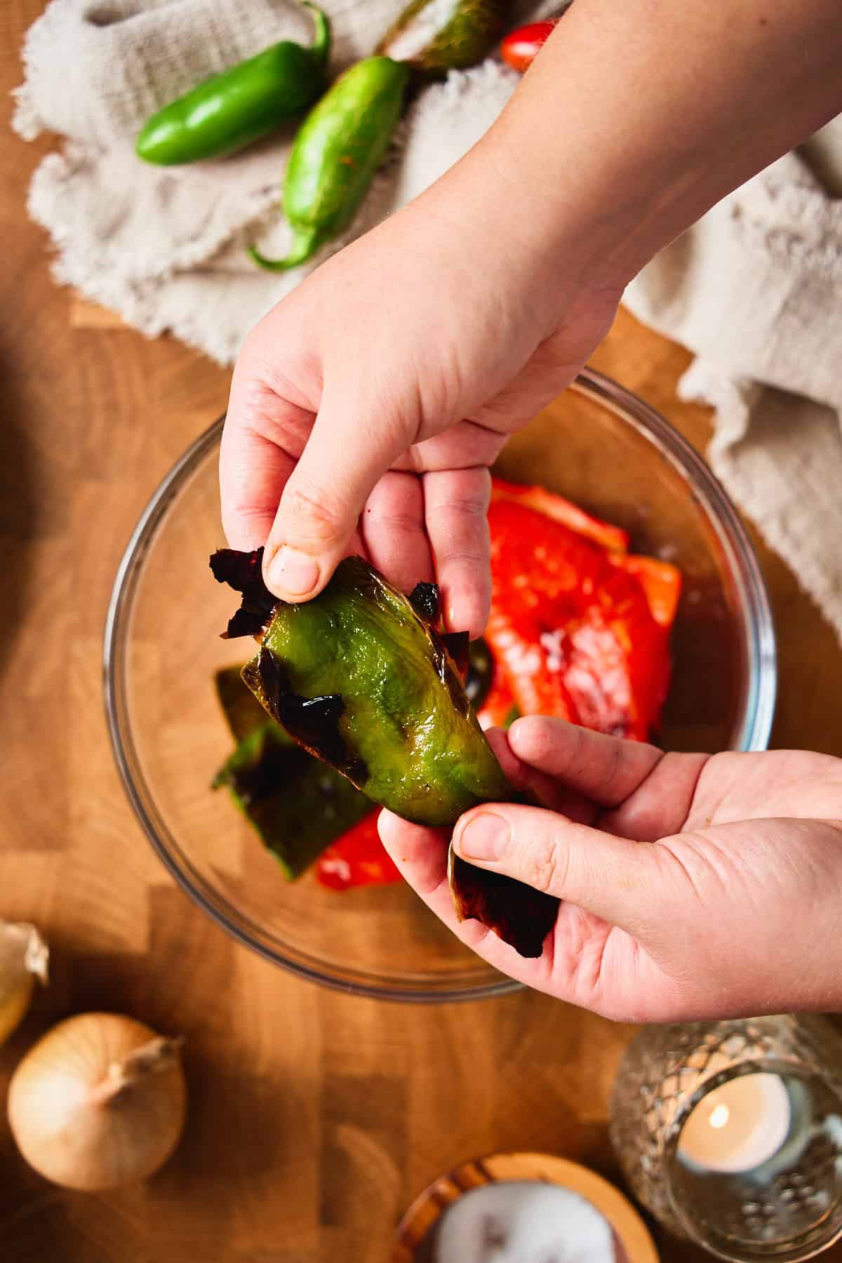 Hands peeling the charred skin off a roasted green jalapeño over a bowl.