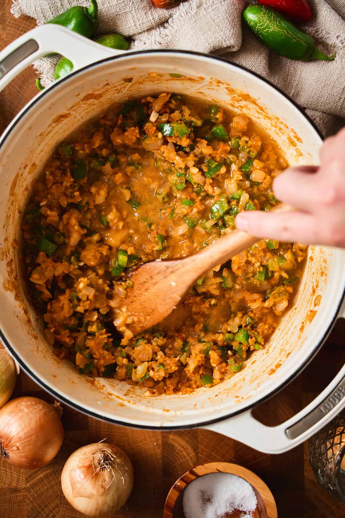 A hand stirring the first splash of stock into the roux with a wooden spoon.