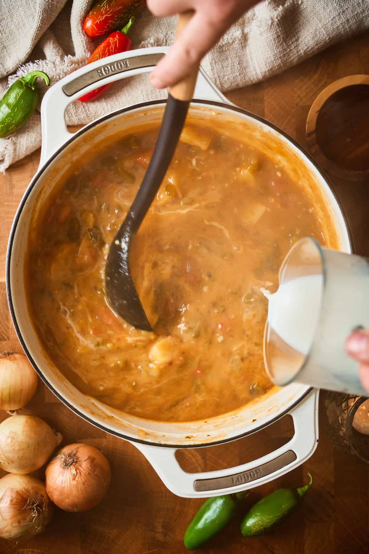 Pouring milk into the jalapeño popper soup base in a white Dutch oven.