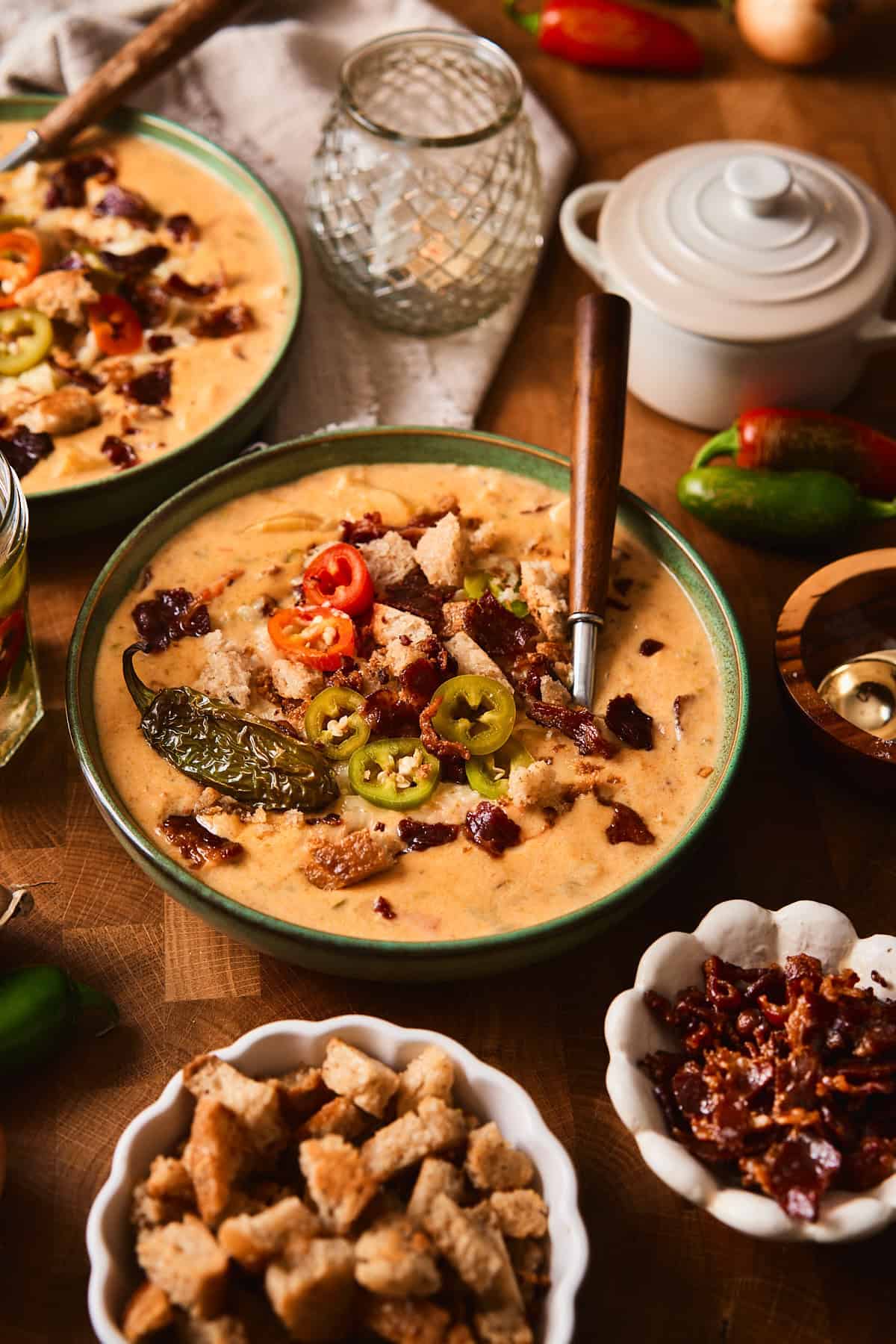 A bowl of creamy jalapeño popper soup topped with roasted jalapeño, pickled jalapeño rounds, croutons, and crispy beef bacon.