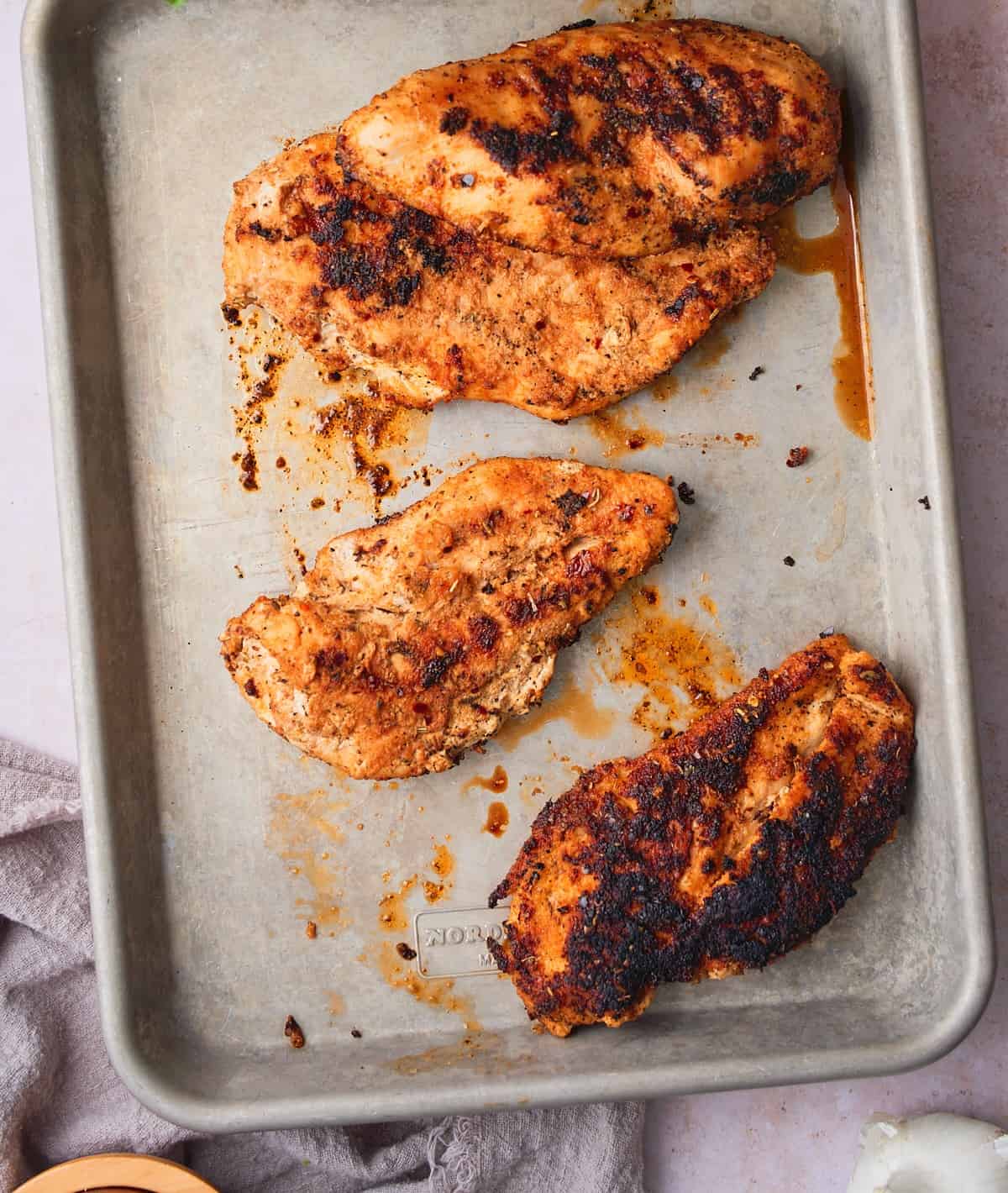 Golden seared seasoned chicken resting on a sheet pan.